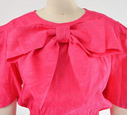 Large pink bow on the neckline of dress.